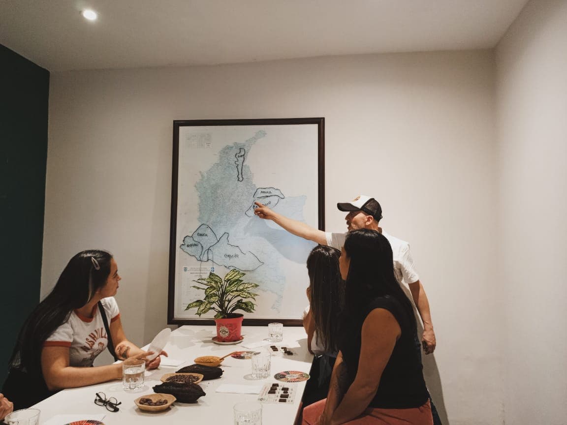 El guía señala las regiones cacaoteras en un mapa de Colombia mientras el grupo cata chocolates en la mesa