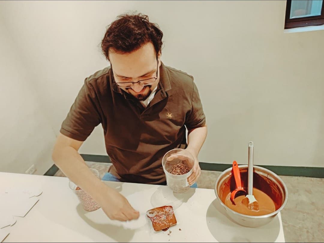 Un participante decora con chispas su propia barra de chocolate junto al bol de chocolate templado